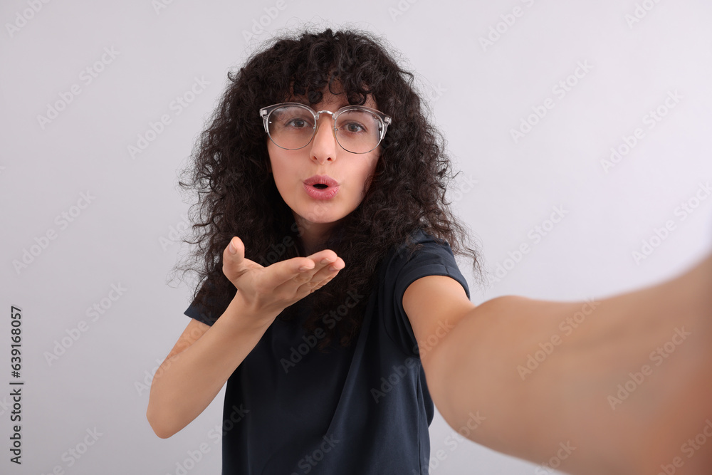 Beautiful young woman in eyeglasses taking selfie on light grey background Beautiful young woman in eyeglasses taking selfie on light grey background