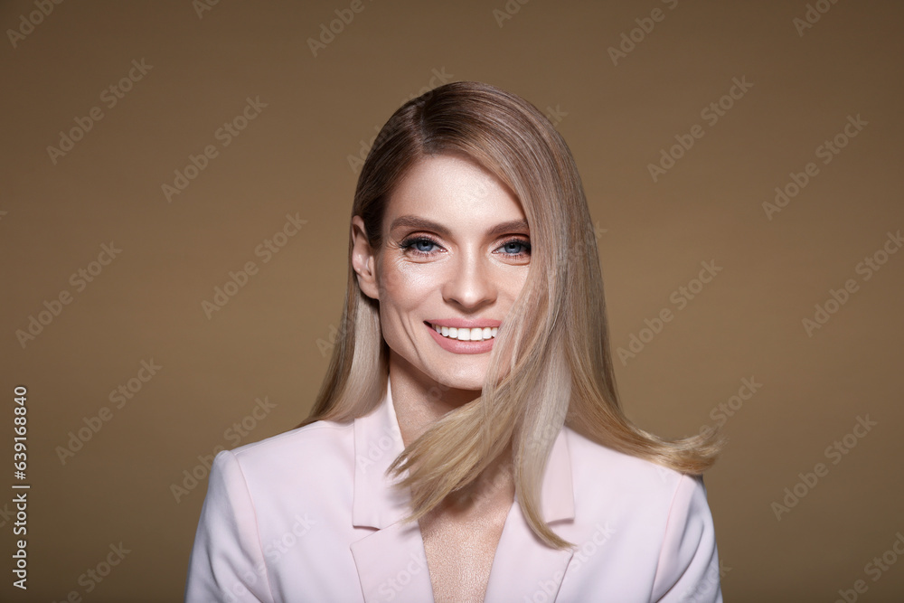 Fototapeta premium Portrait of stylish attractive woman with blonde hair smiling on pastel brown background