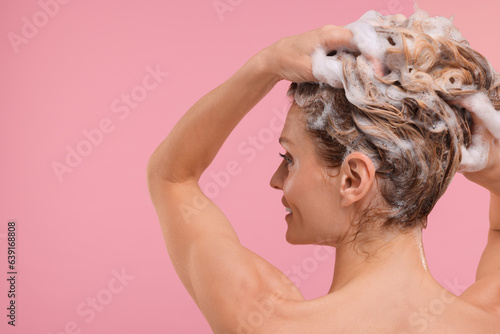 Woman washing hair on pink background, back view. Space for text