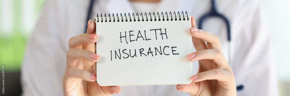 Female doctor shows notepad with words health insurance close up. Female doctor shows notepad with words health insurance close up.