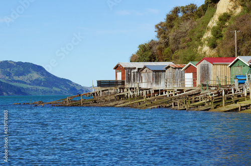 Foto Colourful row of boathouses and boat ramps in a Devauchelle Bay surrounded by bush-covered hills, Onewa, Banks Peninsula, New Zealand