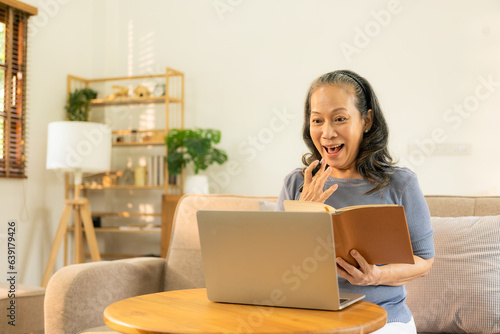 Happy old woman working on her laptop at home. Staying at home. Working from home. Happy middle aged senior woman sitting at desk at home working using laptop computer.