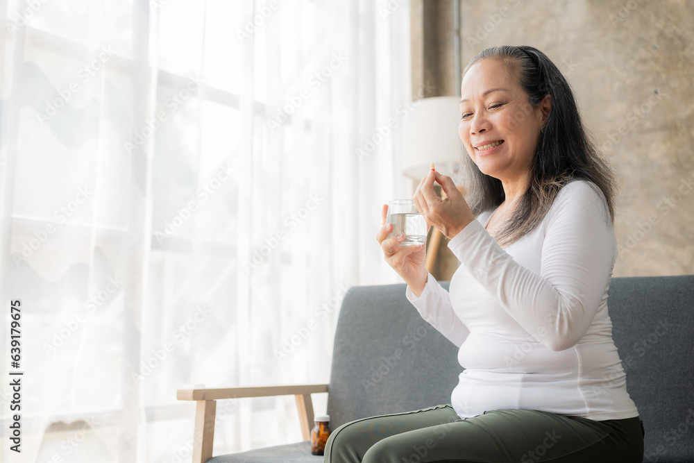 Elderly, unhealthy Asian woman holding a pill bottle reading medication instructions on the package. Sick woman holding pill bottle and reading pill label and watching medication side effects at home, Elderly, unhealthy Asian woman holding a pill bottle reading medication instructions on the package. Sick woman holding pill bottle and reading pill label and watching medication side effects at home,