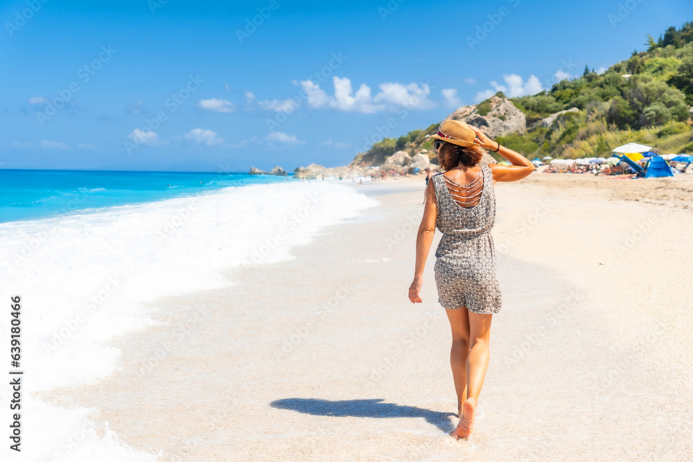 Woman walking along the sea at Megali Petra beach with turquoise water of Lefkada island, Ionian Sea, Greece Woman walking along the sea at Megali Petra beach with turquoise water of Lefkada island, Ionian Sea, Greece
