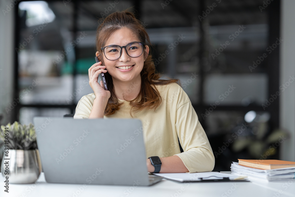 Asian businesswoman or freelancer using laptop computer and mobile phone to communicate with colleague in explaining online meeting or online training. office paperwork Asian businesswoman or freelancer using laptop computer and mobile phone to communicate with colleague in explaining online meeting or online training. office paperwork