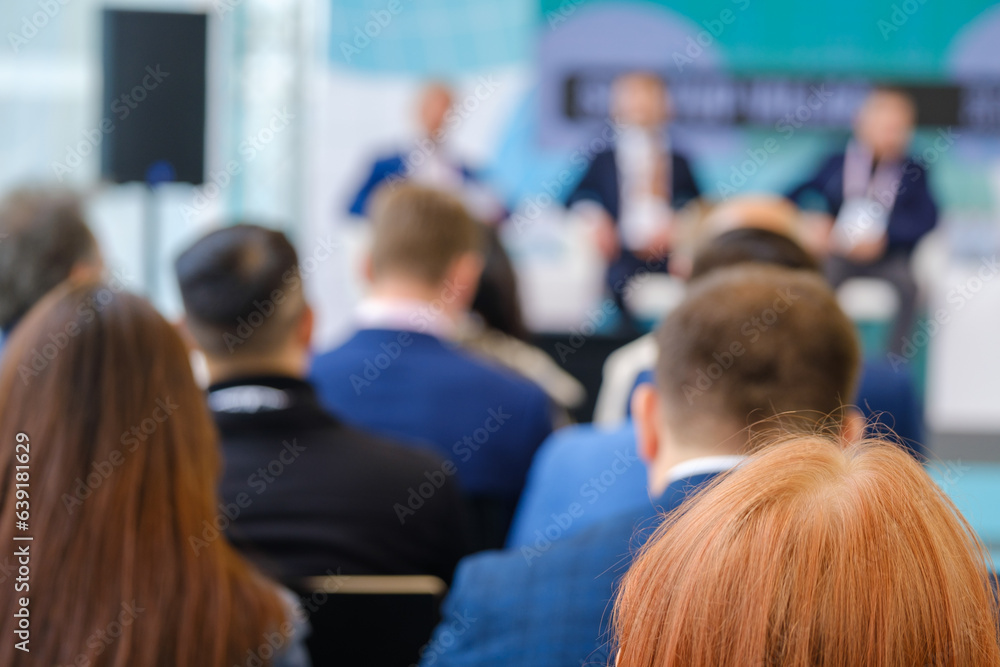 Unrecognizable businesspeople in formal clothes sitting on chairs and listening to male speakers during seminar in modern conference center