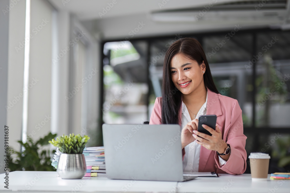 Young businesswoman using phone while sipping coffee in office. Young businesswoman using phone while sipping coffee in office.