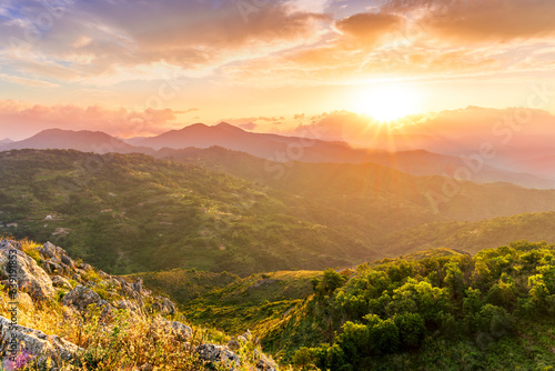 highland mountain landscape of beautiful sunset or sunrise with nice mountain peaks and slopes, green and golden hills and majestic cloudy sky on background