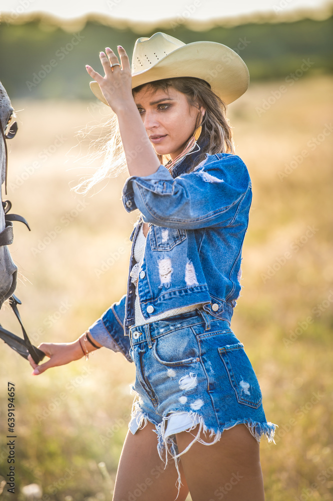 Beautiful blonde woman with curly hair with white hat and horse. Portrait of a girl with denim and her horse. Beautiful girl interacting and having fun with a horse at the ranch