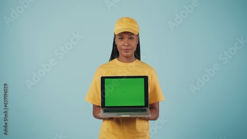 Delivery woman in uniform holding laptop in hands and looking at camera. Advertising area, workspace mockup. photo