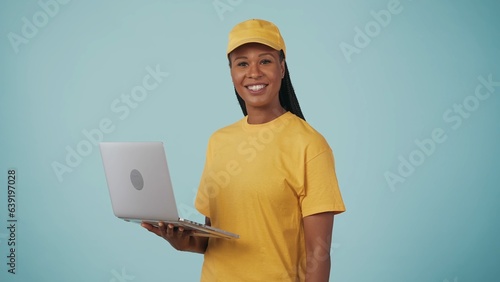 Delivery woman in yellow uniform holding laptop and smiling to the camera. Isolated on blue background. photo