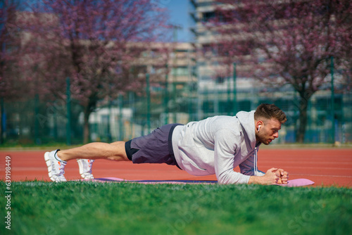 Confident sportsman in earphones doing plank exercises on a fitness mat