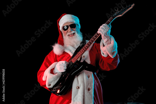 Santa Claus playing the electric guitar in a nightclub at a Christmas and New Year party or Corporate events. Senior guitar player as Santa at a rock concert, festival, or celebration
