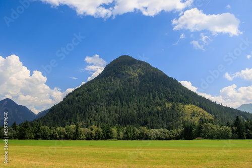An evenly cone-shaped mountain covered with trees up to the summit on a sunny day with blue sky near Heiterwang in Austria