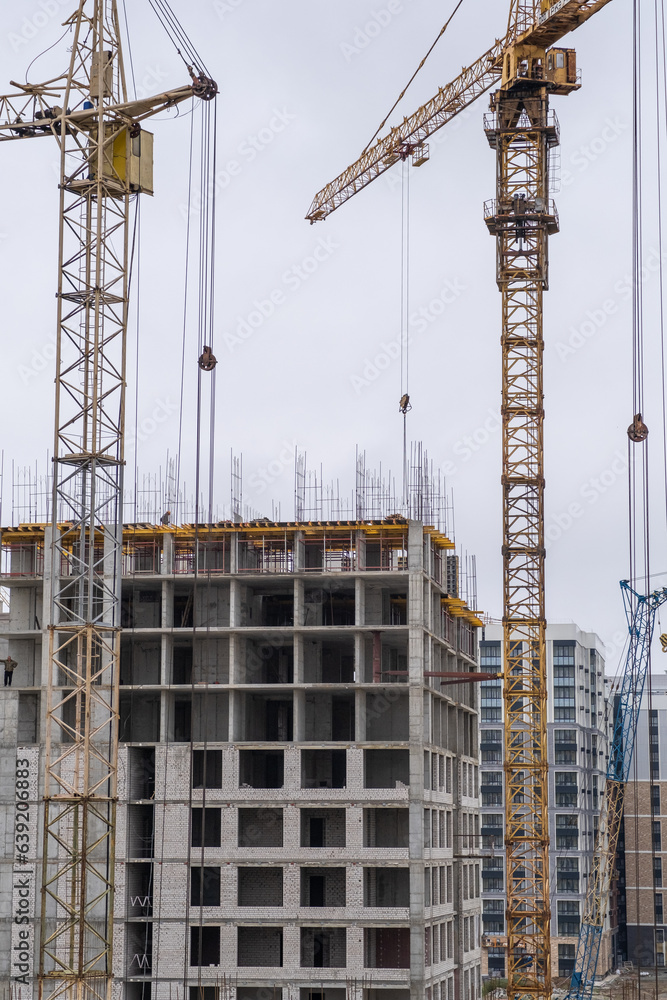 A crane and a building under construction against a blue sky background. Builders work on large construction sites, and there are many cranes working in the field of new construction.