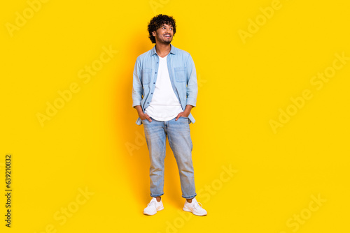 Full length photo of cheerful man with wavy hairstyle wear jeans shirt look at promotion empty space isolated on yellow color background