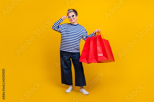 Full length photo of lovely cheerful lady wear cool outfit hold packages special seasonal offer sale isolated on yellow color background