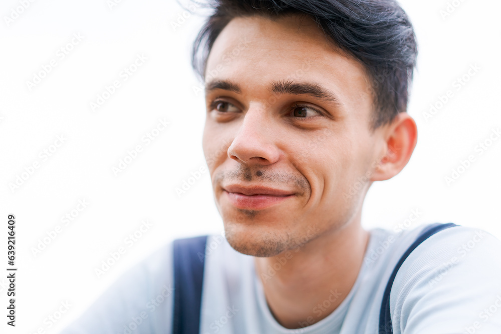 a young guy against the background of the sky looks away and smiles