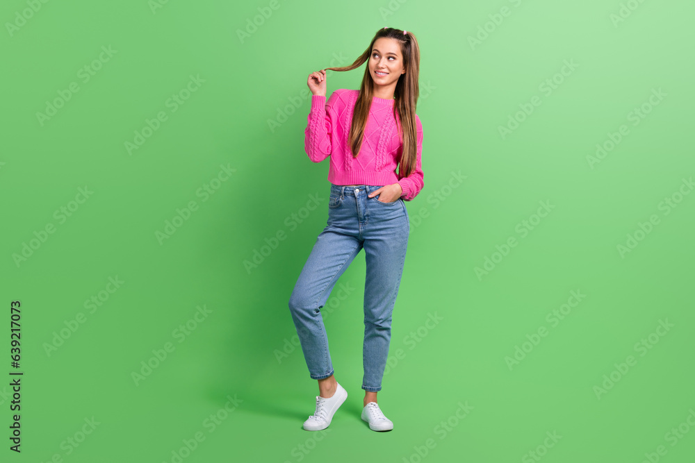 Full length photo of good mood pretty woman dressed pink sweater look at offer empty space touch curl isolated on green color background Full length photo of good mood pretty woman dressed pink sweater look at offer empty space touch curl isolated on green color background
