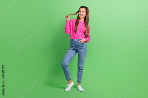 Full length photo of good mood pretty woman dressed pink sweater look at offer empty space touch curl isolated on green color background