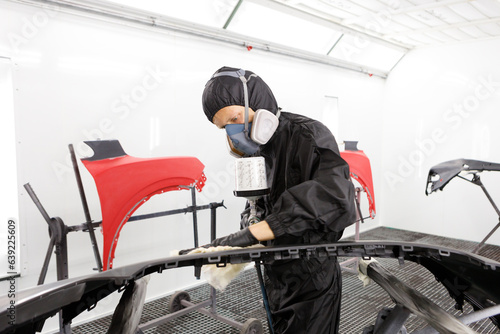 mechanic worker painting a car in a special painting box, wearing a full body costume and protection gear