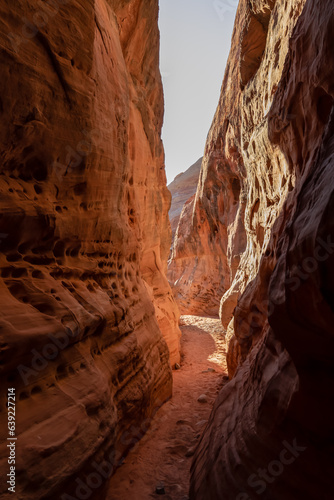 Hike in the narrow Kaolin Wash slot canyon along White Domes Hiking Trail in Valley of Fire State Park in Mojave desert, Nevada, USA. Massive rugged cliffs of striated red and white rock formations