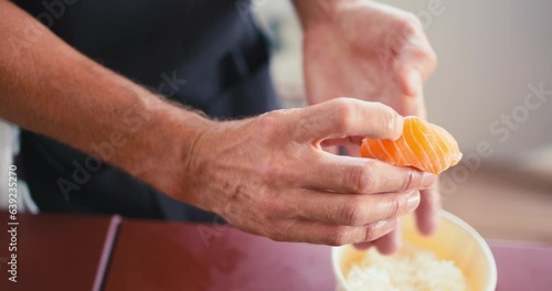 A professional chef combines a rice ball with a piece of salmon and presses them together, making salmon nigiri, traditional Japanese cuisine
