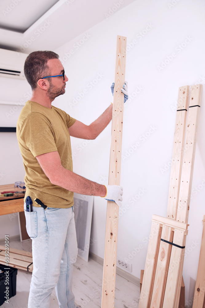 Man assembling new wooden shelf and furniture in the apartment.