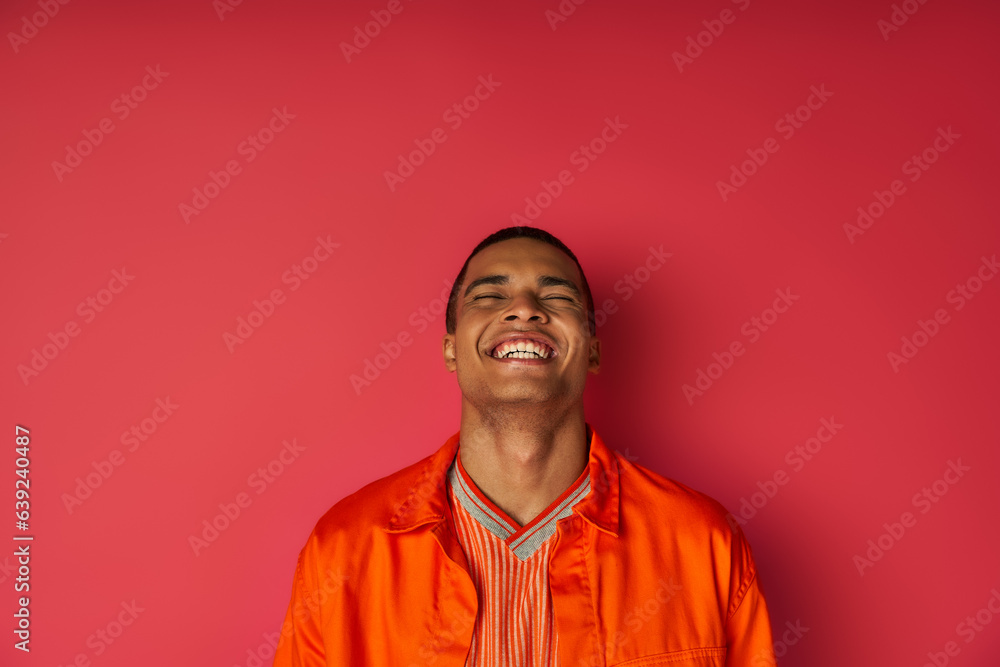 overjoyed african american man in orange shirt laughing with closed eyes on red, excitement overjoyed african american man in orange shirt laughing with closed eyes on red, excitement