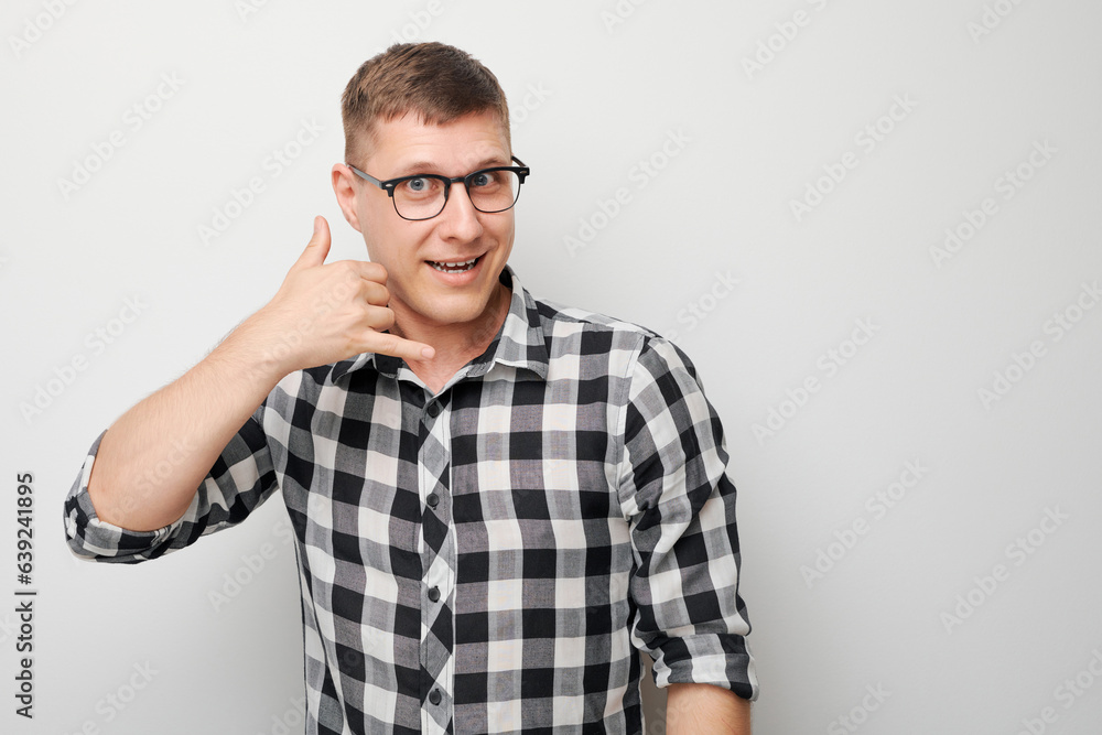 Portrait of young man pretends calling someone, makes call me gesture sign with fingers isolated on white studio background. Give me a call, hand shaped like phone Portrait of young man pretends calling someone, makes call me gesture sign with fingers isolated on white studio background. Give me a call, hand shaped like phone