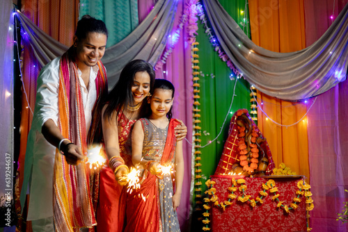 Indian family in ethnic wear celebrating Diwali with firecrackers at home with ganesha Statue in behind