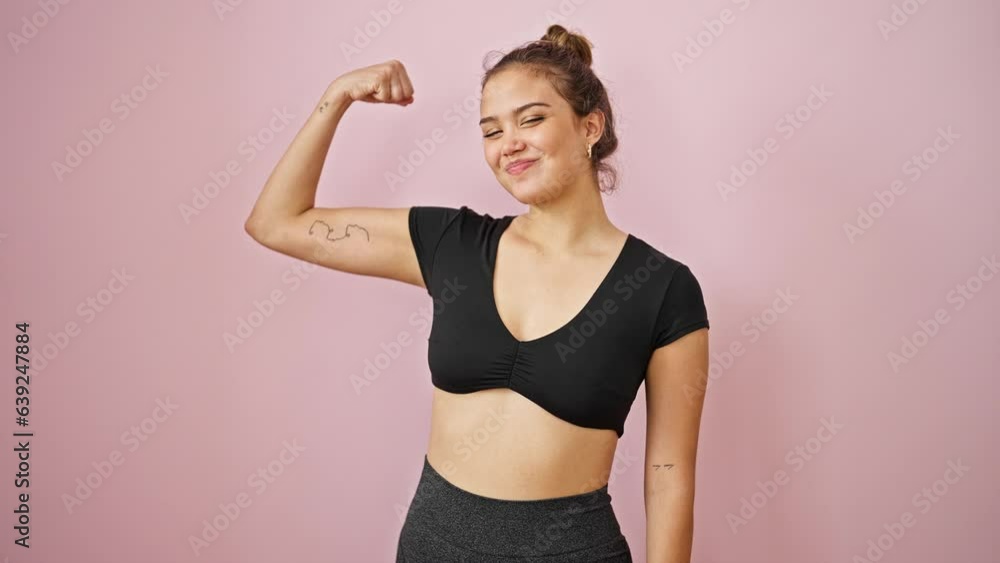 Young beautiful hispanic woman wearing sportswear doing strong gesture with arm over isolated pink background Young beautiful hispanic woman wearing sportswear doing strong gesture with arm over isolated pink background