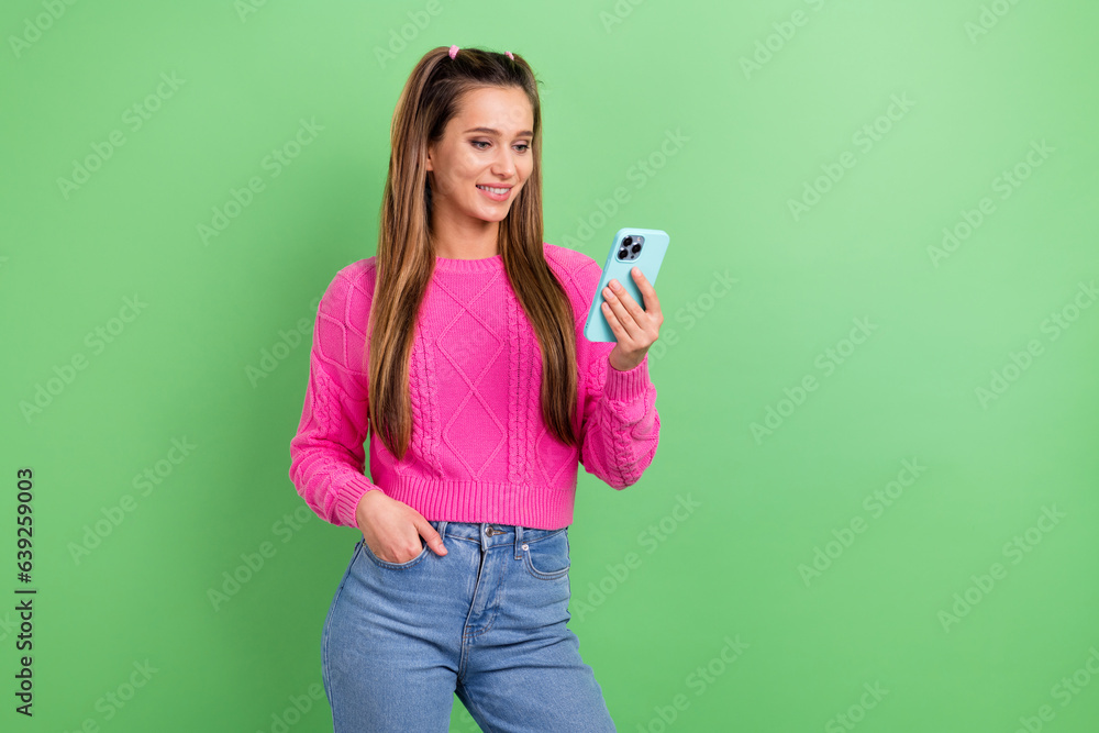 Portrait of good mood girl with stylish hairdo wear knit pullover look at smartphone read email isolated on green color background Portrait of good mood girl with stylish hairdo wear knit pullover look at smartphone read email isolated on green color background