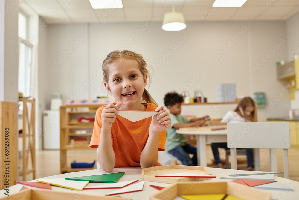 positive child holding wooden triangle and looking at camera in montessori school positive child holding wooden triangle and looking at camera in montessori school
