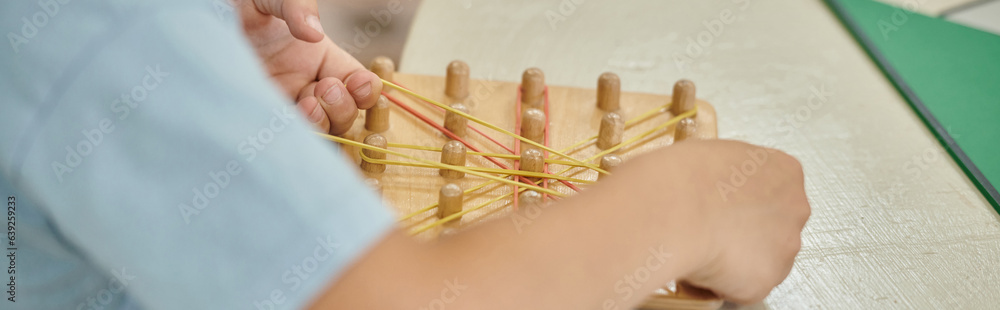 partial view of boy playing with wooden sticks and rubber bands in montessori school, banner partial view of boy playing with wooden sticks and rubber bands in montessori school, banner