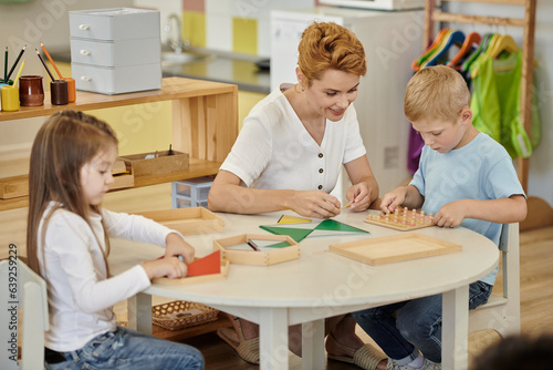smiling teacher playing with kids and didactic materials on table in montessori school