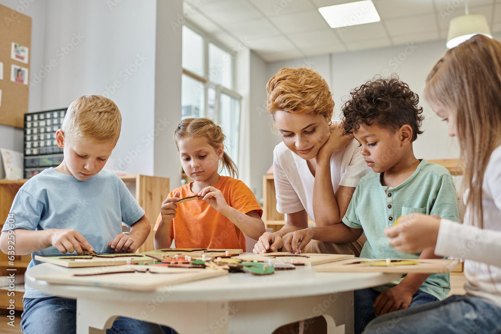 interracial children playing game near teacher in class in montessori school interracial children playing game near teacher in class in montessori school
