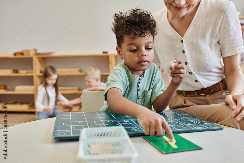 cheerful teacher observing african boy pointing at number near ...