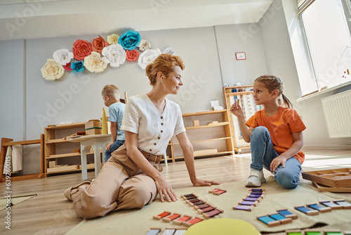 color matching game, girl showing piece of montessori material to happy female teacher, educational photo