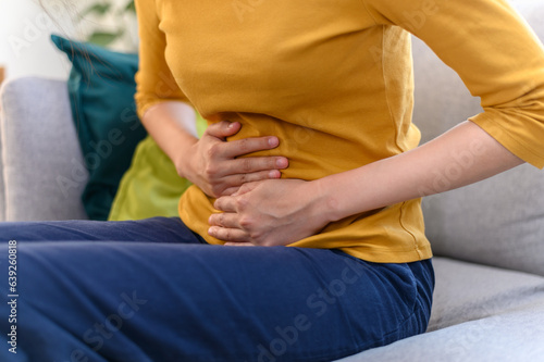 Healthcare medical or daily life concept : Close up hands of young Asian woman holding stomach have a stomachache or menstruation pain sitting on her sofa.