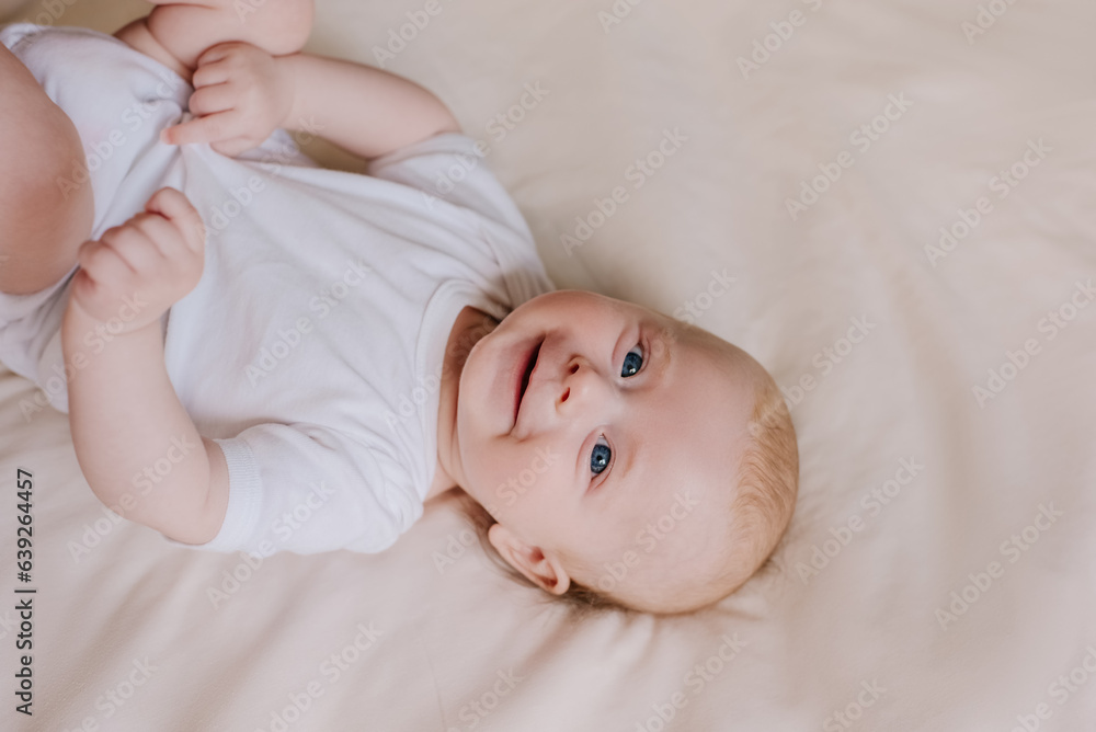 Portrait of cute newborn baby son lying down on comfortable bed at home. Pretty smiling infant boy in white bodysuit rests on bedsheets, Infancy, healthcare and paediatrics, babyhood concept Portrait of cute newborn baby son lying down on comfortable bed at home. Pretty smiling infant boy in white bodysuit rests on bedsheets, Infancy, healthcare and paediatrics, babyhood concept