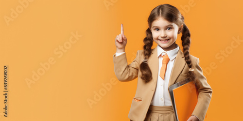 Cheerful happy young small schoolgirl points up with her index finger and standing in front of isolated pale orange background.Created with Generative AI technology.