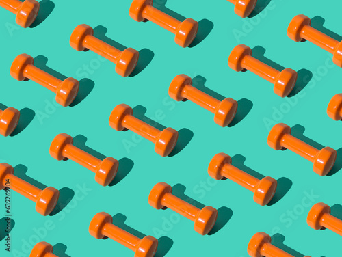 Creative pattern composition made of orange dumbbells on pastel green background. Minimal fitness, healthy lifestyle and sport concept. Trendy exercise and fitness backround idea. © Jakov Ilkoski