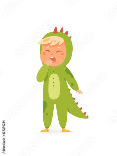 Cute sleepy boy in crocodile costume yawning at pajama party, kid in kigurumi overalls