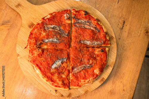 Pizza tonda cotta nel ruoto in un forno elettrico condita con sugo di pomodoro, olio, acciughe e origano e fotografata su un tagliere di legno photo