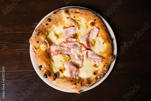 Pizza gourmet napoletana con mozzarella, pancetta e formaggio fotografata dall'alto su un tavolo di legno 