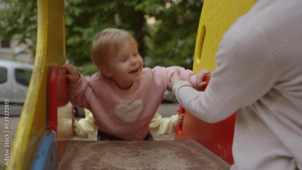 Little happy girl with her mom have fun on the playground. 1.9 year old toddler on a slide. Healthy summer activity for children. Little happy girl with her mom have fun on the playground. 1.9 year old toddler on a slide. Healthy summer activity for children.