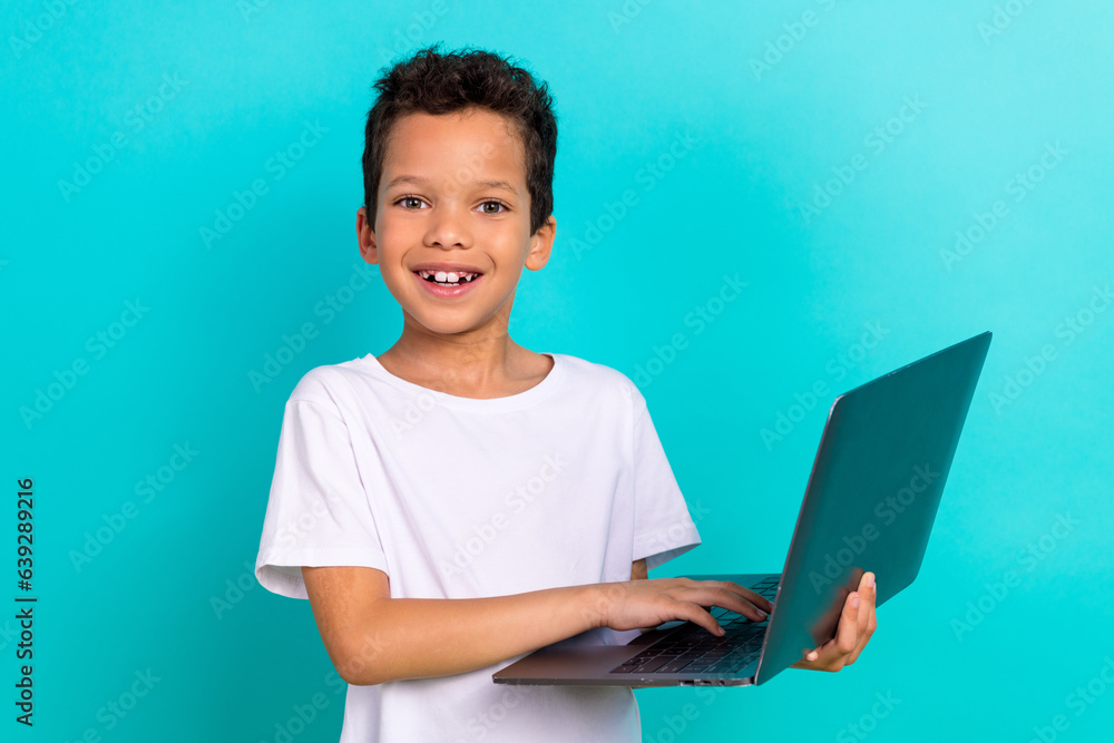 Photo of cheerful little schoolkid beaming smile hold use wireless netbook isolated on teal color background Photo of cheerful little schoolkid beaming smile hold use wireless netbook isolated on teal color background