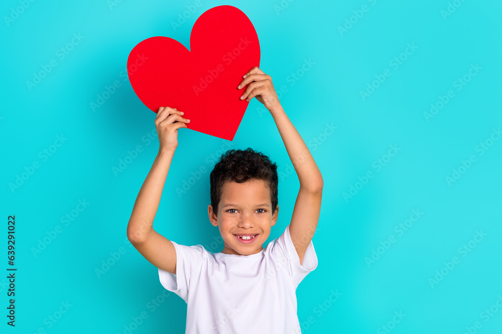 Photo of sweet positive boy toothy smile hands hold red paper heart empty space ad isolated on teal color background Photo of sweet positive boy toothy smile hands hold red paper heart empty space ad isolated on teal color background