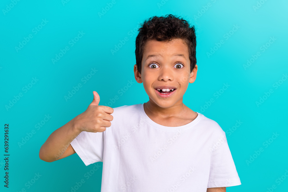 Photo of surprised amazed boy wear trendy white clothes thumb up wow cool special offer shop sale isolated on cyan color background Photo of surprised amazed boy wear trendy white clothes thumb up wow cool special offer shop sale isolated on cyan color background